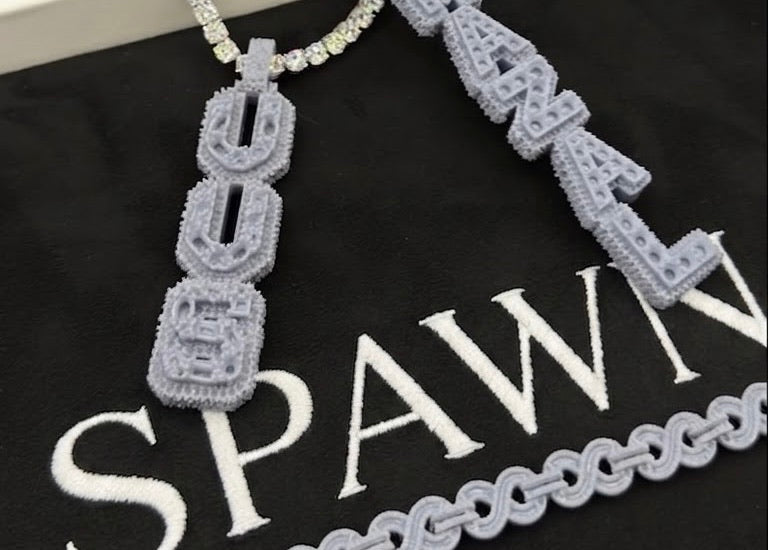 Grey resin moulds of the letter pendants and a chain, laid on the SPAWN board next to finished tennis chains.